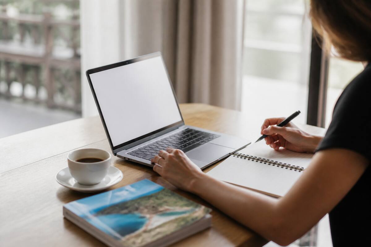 Iemand die op een rustige manier vakanties vergelijkt met laptop en notitieboekje